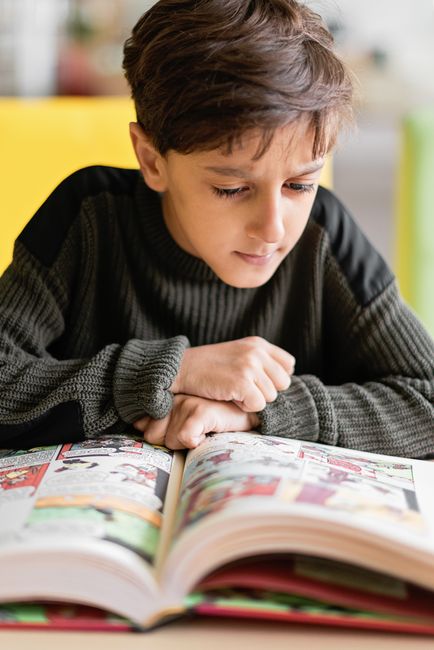 A child concentrates on reading a colorful comic book, capturing curiosity and focus.